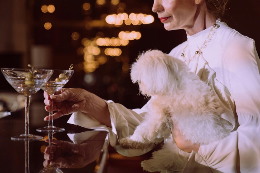 Sophisticated woman holding a white dog while enjoying cocktails at a classy bar setting.